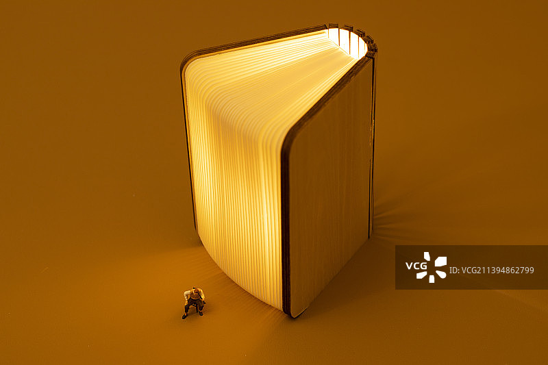 橙色背景下的发光的书和模型小人图片素材
