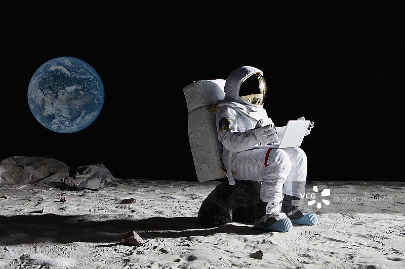 月球上的宇航员坐在一块岩石上用笔记本电脑图片素材
