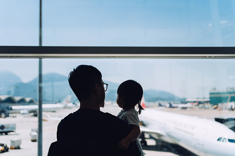 在機場等待起飛的時候，快樂的年輕亞洲父親抱著可愛的小女兒，透過窗戶看著飛機的剪影圖片素材