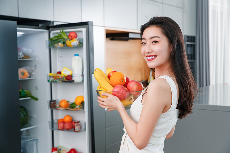 拿著水果的青年女人站在冰箱前圖片素材