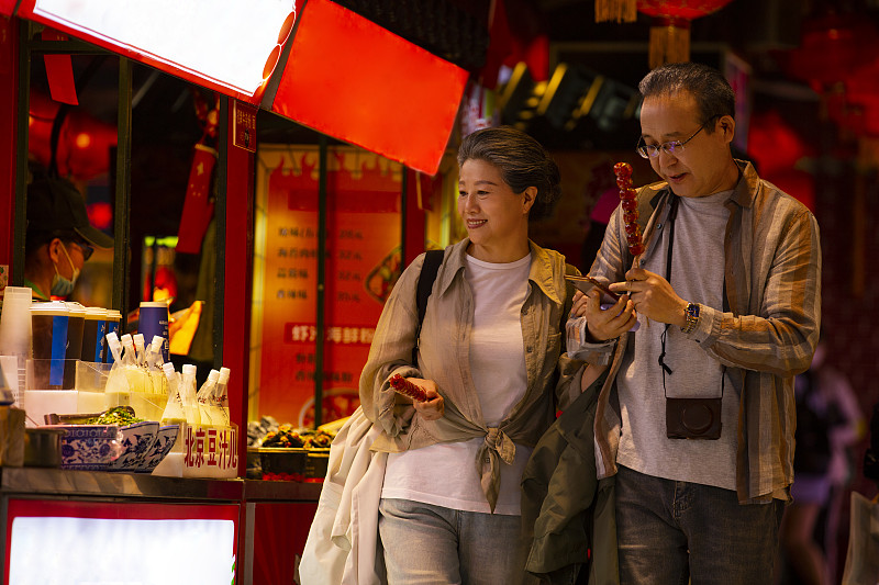 老年人City walk系列:老年夫妇拿着糖葫芦在北京美食街旅行图片下载