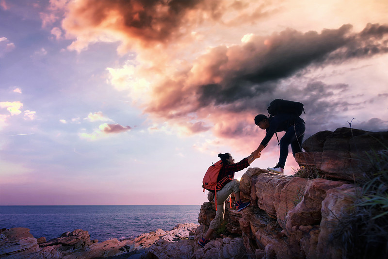 亞洲人伸出手幫助他的朋友上山。團隊合作，幫助，攀登的概念。圖片素材