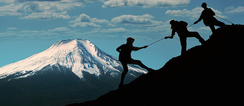年輕的亞洲三名徒步旅行者正在攀登附近一座山的山頂。日出時，人們互相幫助爬山。伸出援手。攀爬。幫助和團隊合作的理念圖片素材