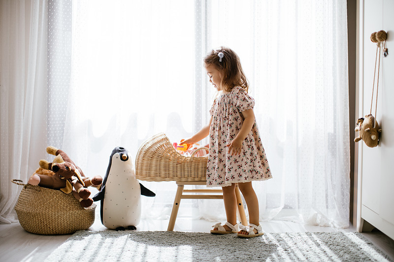 可愛的小女孩在嬰兒床里喂她的玩具娃娃，在有大窗戶的陽光臥室里玩圖片素材