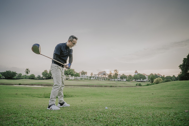 周末，一位成熟的亞洲華人男子在高爾夫球場開球，揮舞著他的球棒圖片素材