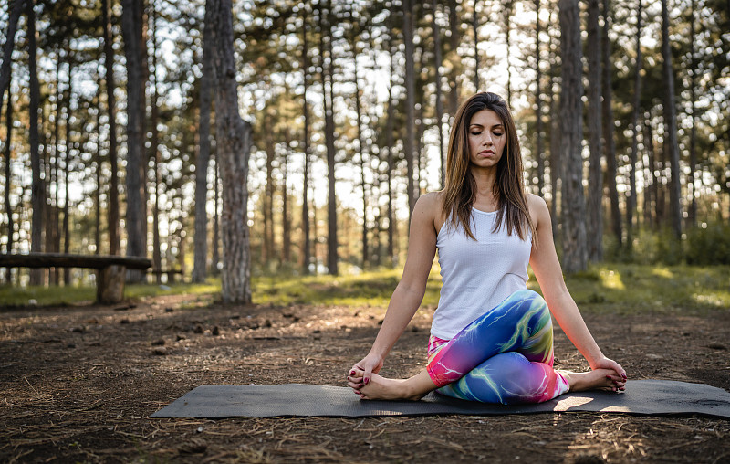 一個高加索婦女在大自然中練習瑜伽，在樹林或公園獨自坐著，健康的生活方式冥想和現代放松抗壓力的概念拷貝空間正面視圖圖片下載