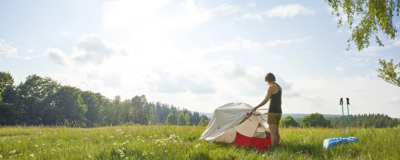 在陽光明媚的日子里，孤獨的女性在茂盛的草地上搭帳篷攝影圖片
