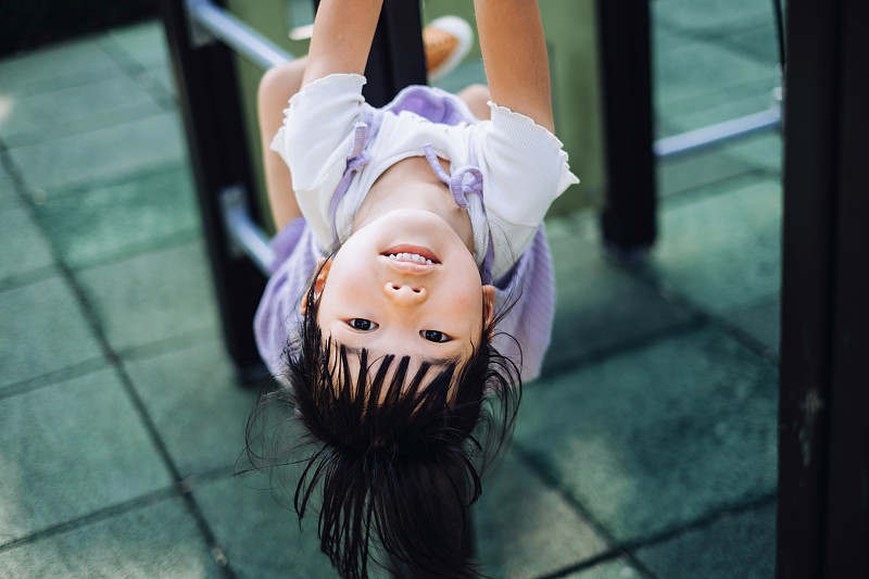 快樂的亞洲小女孩在操場上玩得很開心，倒掛在攀爬架上。看著鏡頭。童年的生活方式。戶外趣味、無憂無慮、自由的理念圖片下載