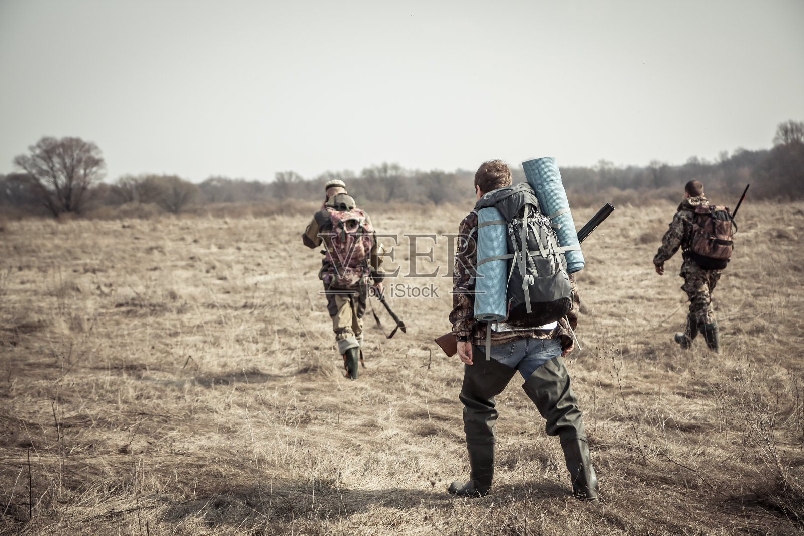 狩猎场景:一群猎人背着背包，背着猎枪，在阴天的狩猎季节穿过乡间田野照片摄影图片