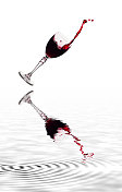 一杯坠入地面的葡萄酒，倒映在水面上。图片素材