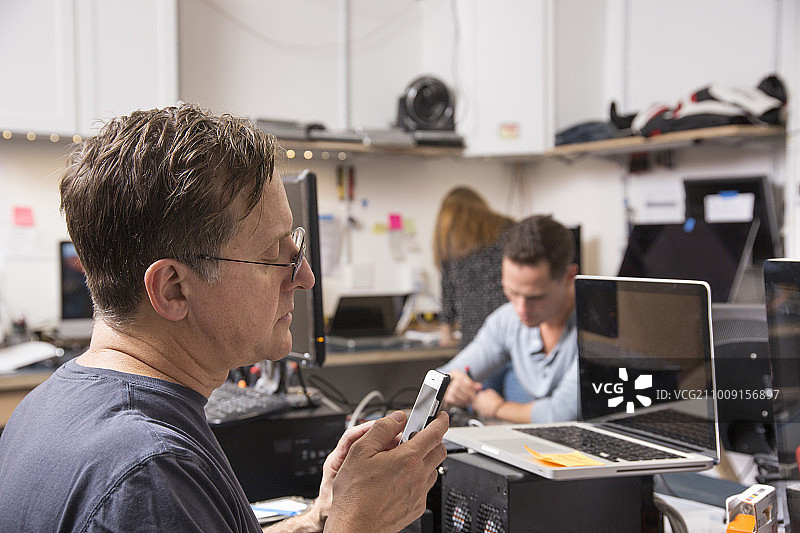 三个人在一个技术实验室工作，一个男人在前景看手机。图片素材