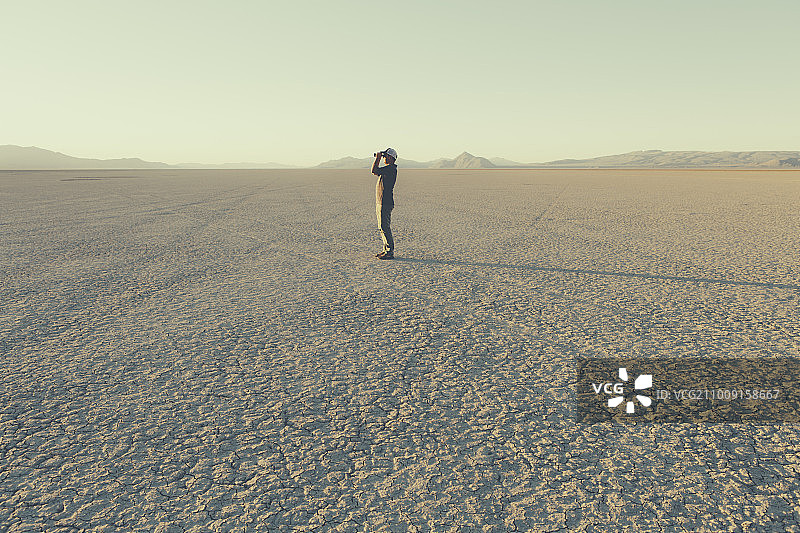 内华达州黑岩沙漠，一名男子站在遥远的沙漠中，用双筒望远镜观察图片素材