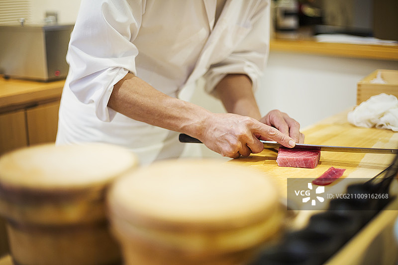 在小型商业厨房工作的厨师，用一把大刀切鱼来做寿司的厨师图片素材