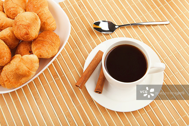 早餐咖啡和牛角面包放在桌子上，背景很亮。图片素材