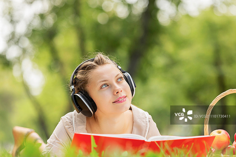 在夏季公园野餐。年轻迷人的女孩戴着耳机在夏季公园图片素材