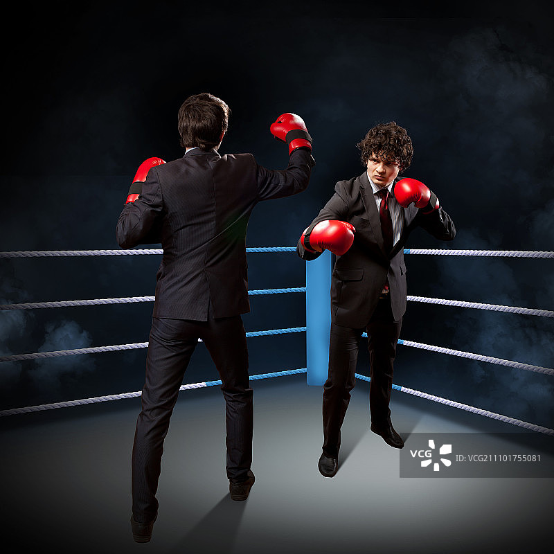 两个年轻的商人在拳击。两个年轻的商人在黑暗的背景下拳击。概念上的拼贴图片素材