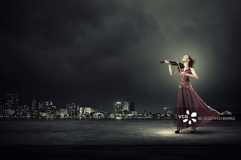 优雅的女孩拉小提琴。年轻的女小提琴手穿着长长的晚礼服图片素材
