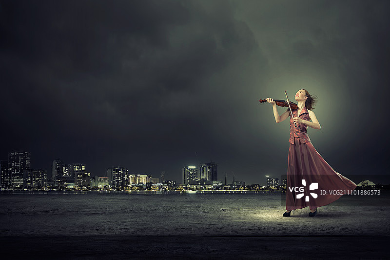 优雅的女孩拉小提琴。年轻的女小提琴手穿着长长的晚礼服图片素材