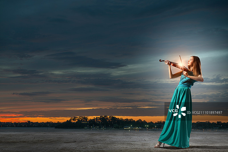 穿着绿色长裙的迷人女子在拉小提琴。优雅的小提琴家的球员图片素材
