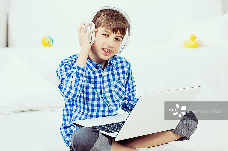 孩子享受闲暇时光。坐在地板上通过耳机听笔记本电脑音乐的学龄期男孩图片素材