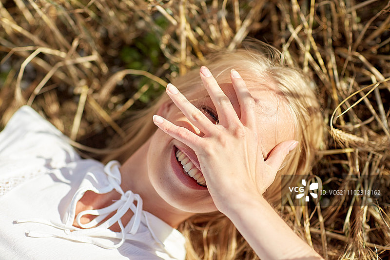 自然，暑假，假期和人的概念-近距离幸福年轻女子躺在谷物田和覆盖脸的手图片素材
