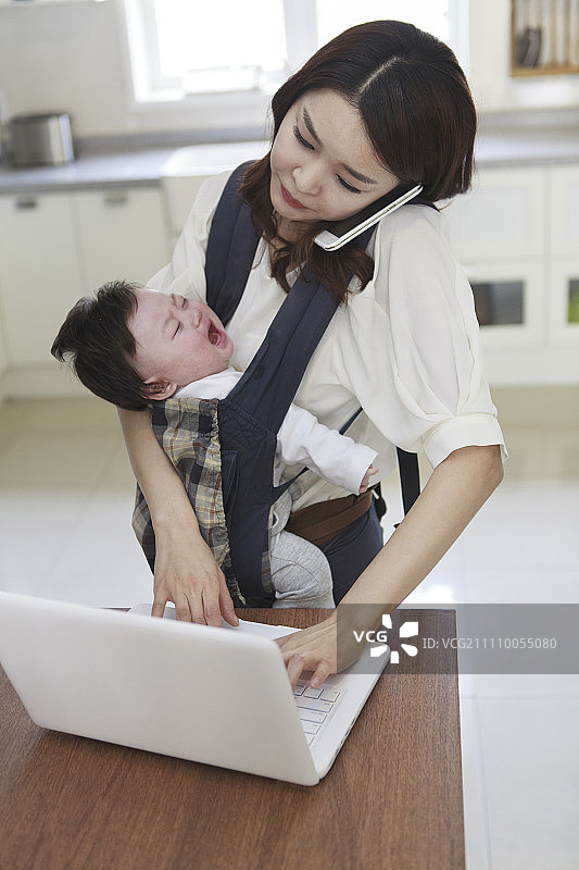 接电话的商人抱着哭闹的婴儿用笔记本电脑工作图片素材