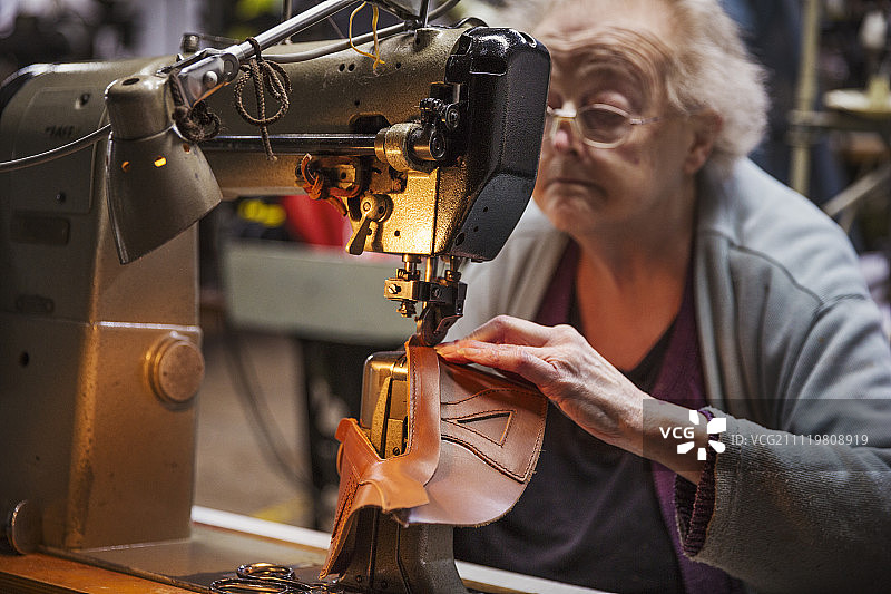 一位老妇人坐在鞋厂的缝纫机旁。图片素材
