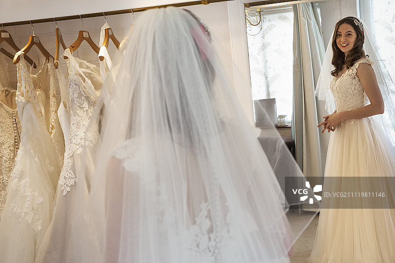 在一家婚礼精品店里，一位穿着白色婚纱的年轻女子看着镜子里自己的倒影。图片素材