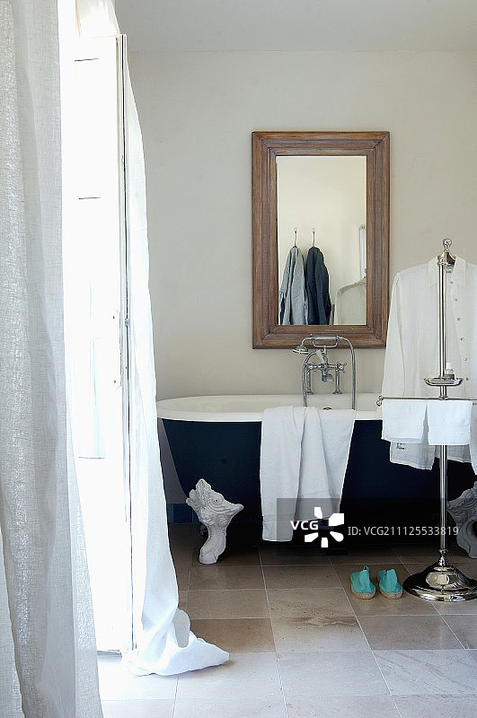 在现代室内，毛巾和男式衬衫放在复古的爪足浴缸前面，下面是镶框的镜子图片素材