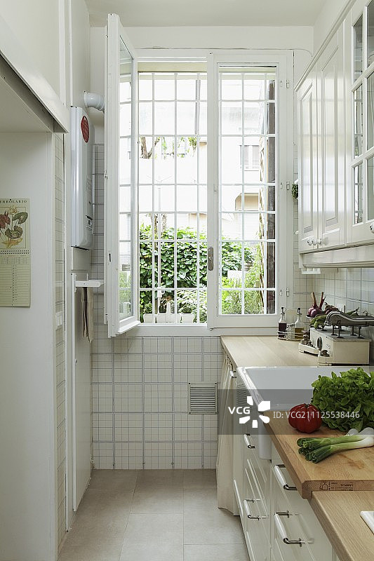 厨房柜台上的蔬菜在狭窄的厨房，远端有开着的铁条窗图片素材
