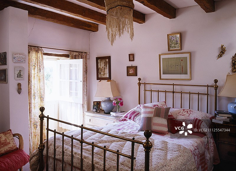 历史农舍的浪漫卧室里，手工缝制的棉被和散落的靠垫在黄铜床上图片素材