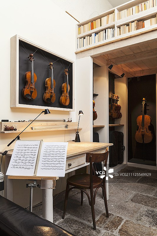在乐器制造商的工作室的生活区域，有古董桌子，小提琴在展示柜，音乐架和书柜栏杆图片素材