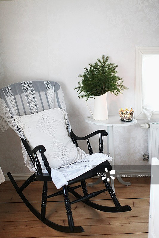 黑漆木制摇椅，白色靠垫，旁边是水罐的冷杉枝放在边桌上图片素材