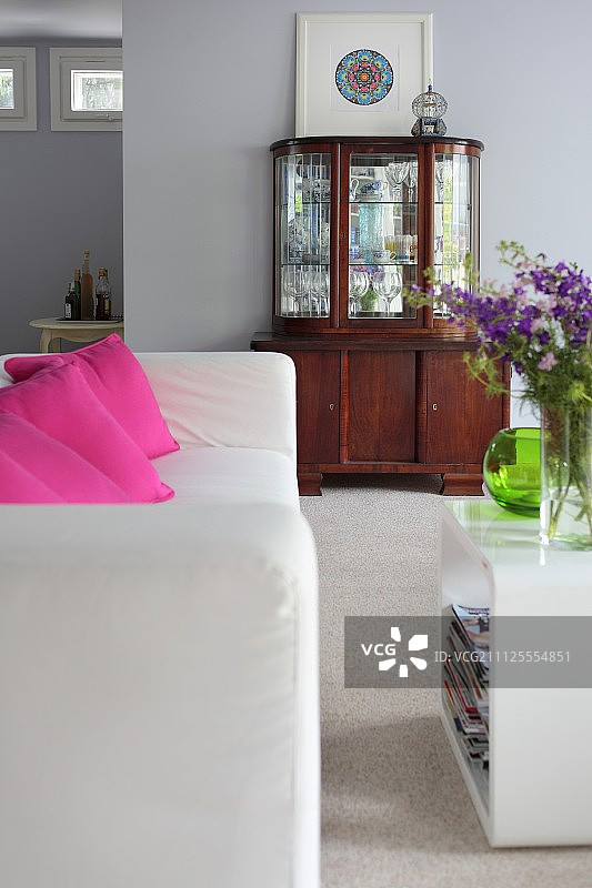 白色沙发，粉色散垫，塑料边桌;背景靠墙的古董陈列柜图片素材
