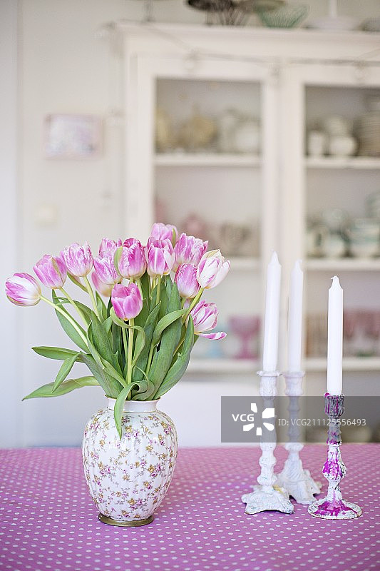 粉白色图案的桌布上，插着粉红郁金香和白色蜡烛的烛台图片素材