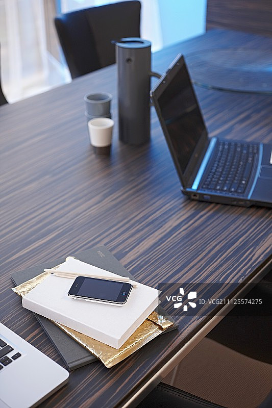 笔记本电脑、保温瓶、书和智能手机放在优雅的异国情调的木质办公桌上图片素材
