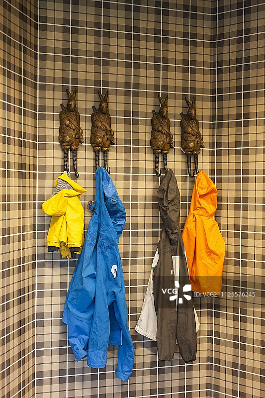 五颜六色的雨衣挂在棕色格子墙上的兔形大衣挂钩上图片素材