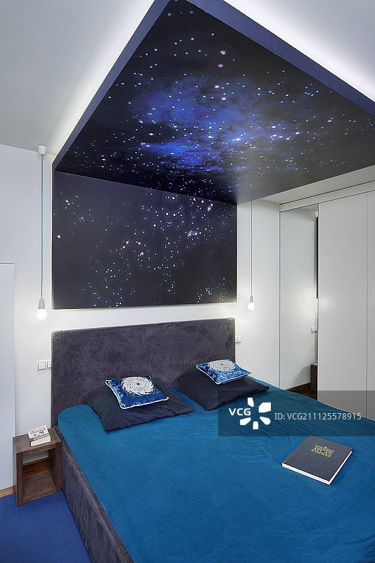 在现代卧室的天花板和墙壁上，双人床上有蓝色的床单，下面是由背光打印玻璃制成的星空顶棚图片素材