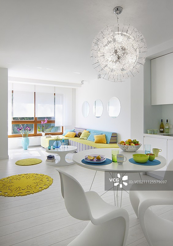 白色的开放式室内，餐桌上放着经典的贝壳椅，下面是星裂吊灯，圆形的黄色地毯提供了泼洒的色彩图片素材