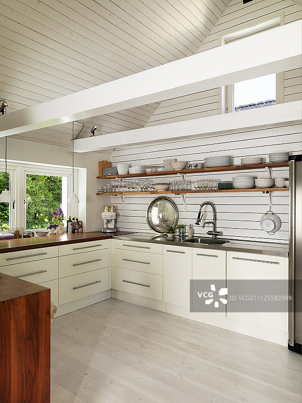 在一所翻新的乡村别墅里，厨房陈设着灰色的现代家具，架子上放着陶器，屋顶横梁是白色的图片素材