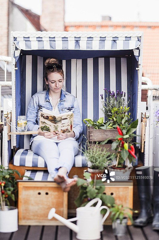 坐在阳台上用植物装饰的沙滩椅上看书的女人图片素材