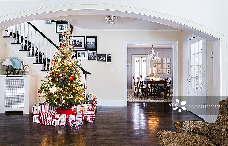 美国乡村别墅宽敞的走廊上，红白相间的礼物在装饰着童话灯的圣诞树下图片素材