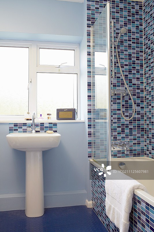 窗台下的基座水槽紧挨着浴缸，靠墙贴着不同色调的蓝色和红色瓷砖图片素材