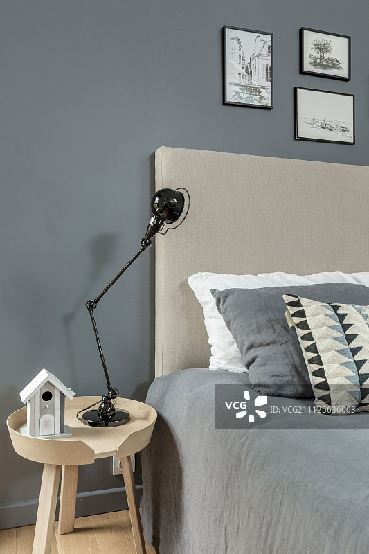 床边的桌子上放着黑色的灯，米色的床头板和灰色的床罩，靠在灰色的墙壁上图片素材