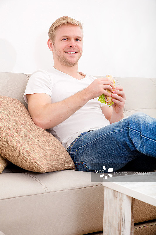 一个年轻人在家里吃三明治图片素材
