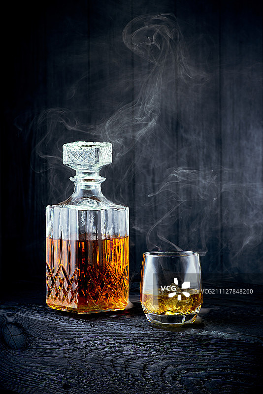 黑木桌上放着一杯威士忌和一瓶水瓶图片素材