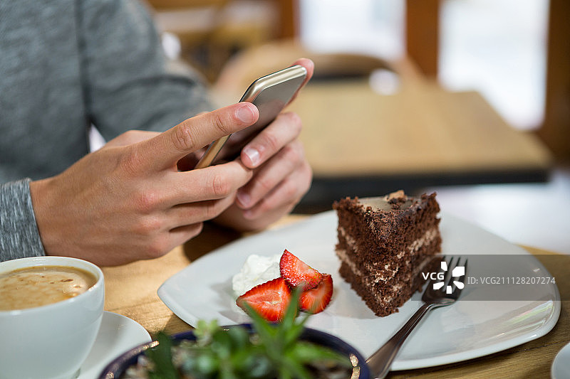 在咖啡馆的桌子上，一个男人用手机端着咖啡和甜点图片素材