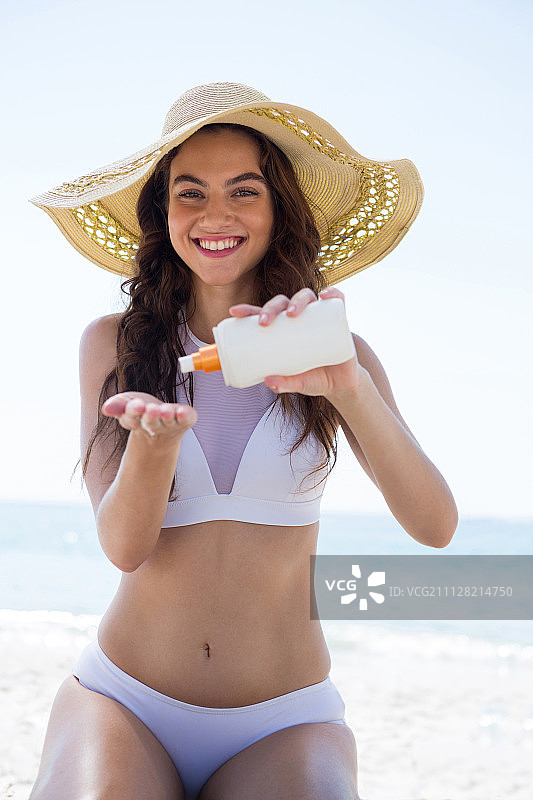 一个微笑的女人跪在沙滩上往手掌上浇奶油的肖像图片素材