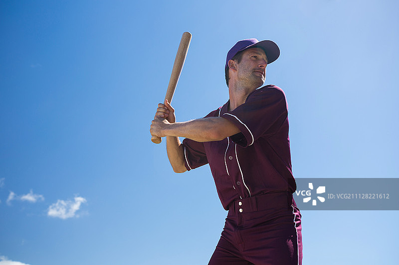 在阳光明媚的日子里，年轻的棒球运动员拿着球棒对抗蓝天的低角度视图图片素材