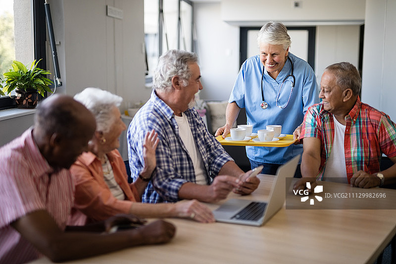 微笑的医护人员在敬老院为坐在桌边的老人端上咖啡图片素材